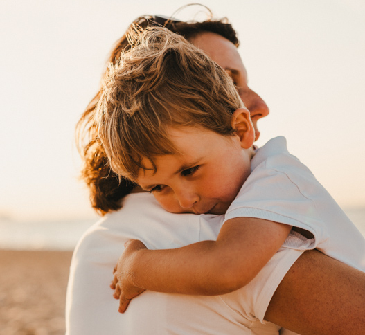 mother carrying a young child across the beach